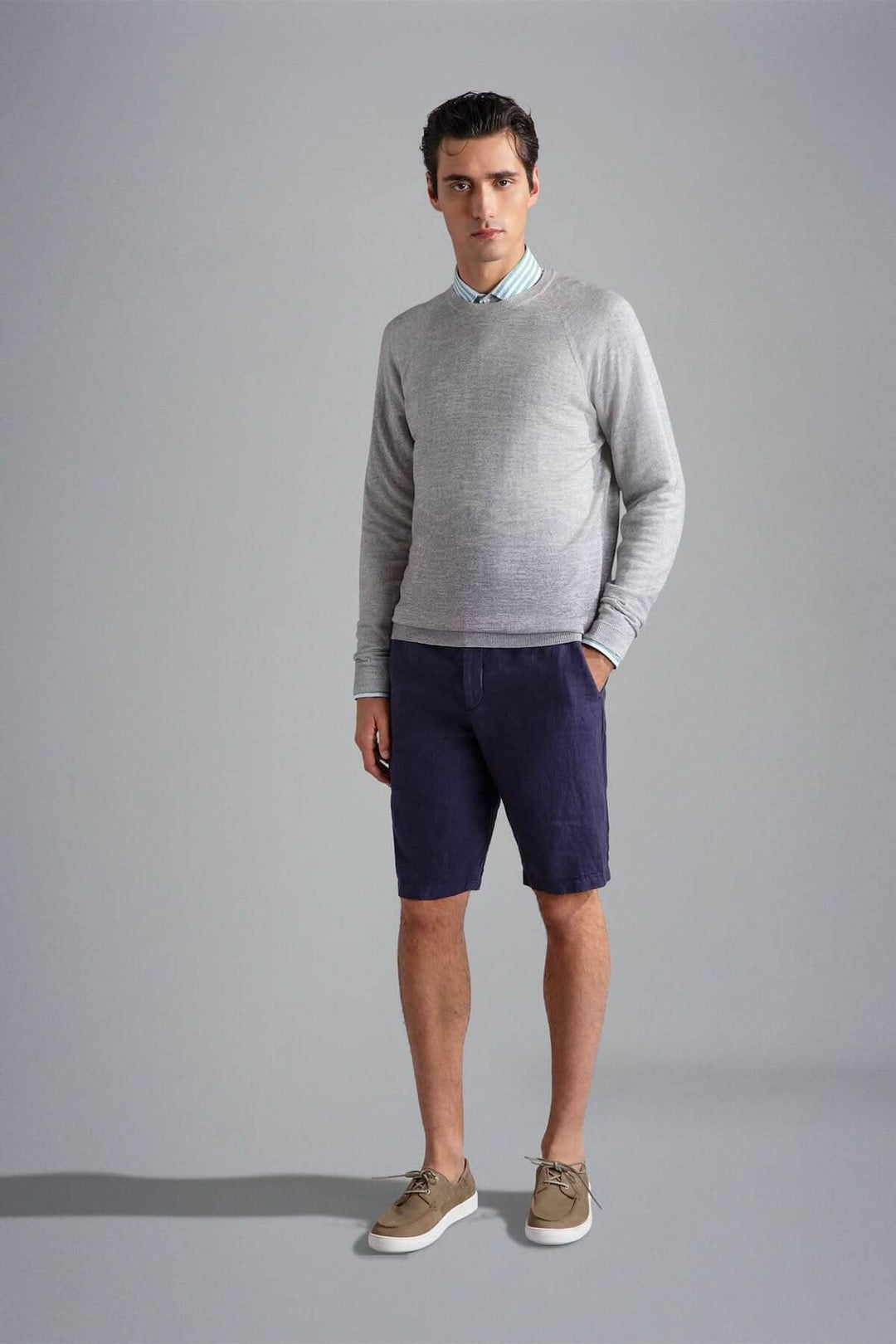 Homme en pull gris, chemise à rayures et short bleu marine, stylé et décontracté.