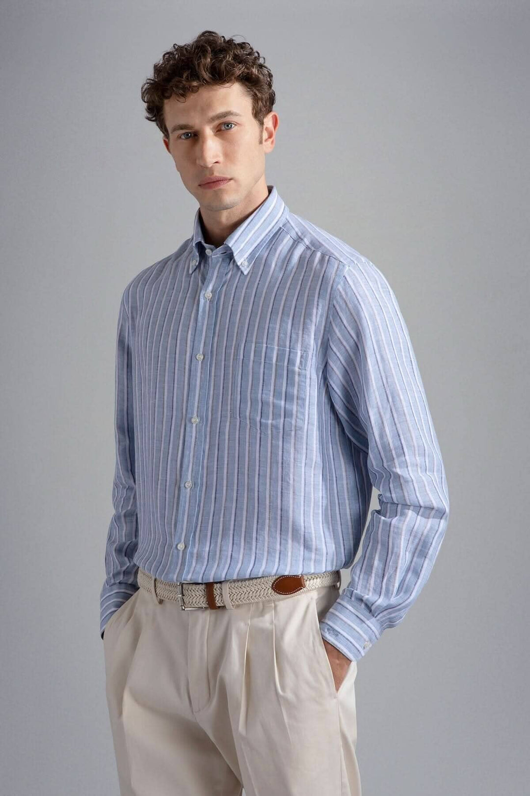Chemise lignée élégante en lin avec des rayures bleues, portée par un homme en pantalon clair, style décontracté.
