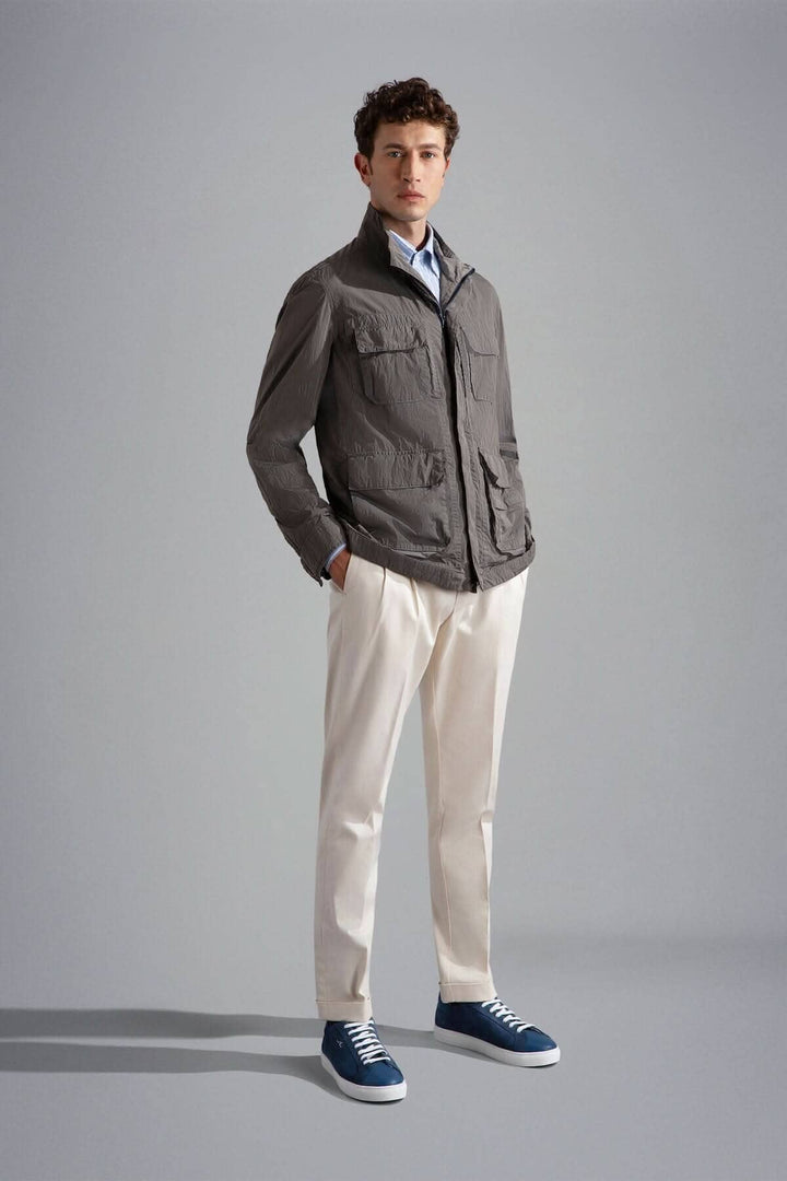 Homme portant une veste grise, chemise light, pantalon beige et baskets bleues dans un environnement moderne.