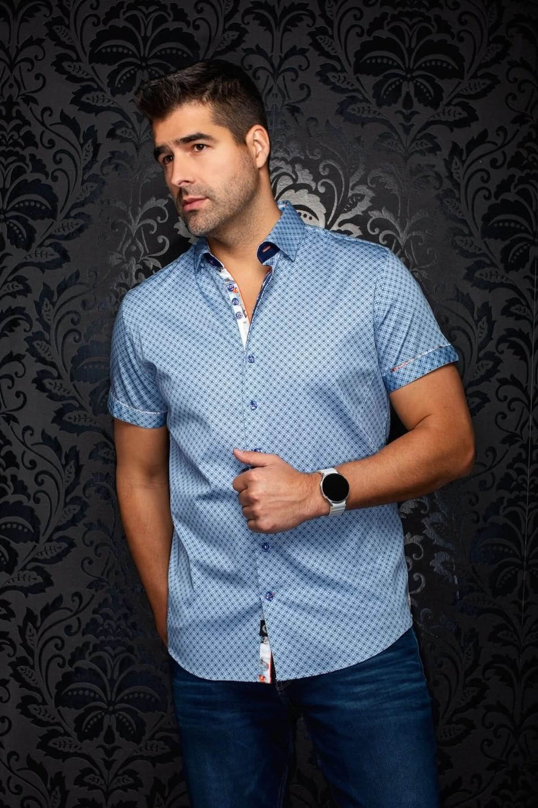 Homme portant la chemise manches courtes ALONA SS avec micro-imprimé, décontracté et élégant, sur fond noir à motifs.