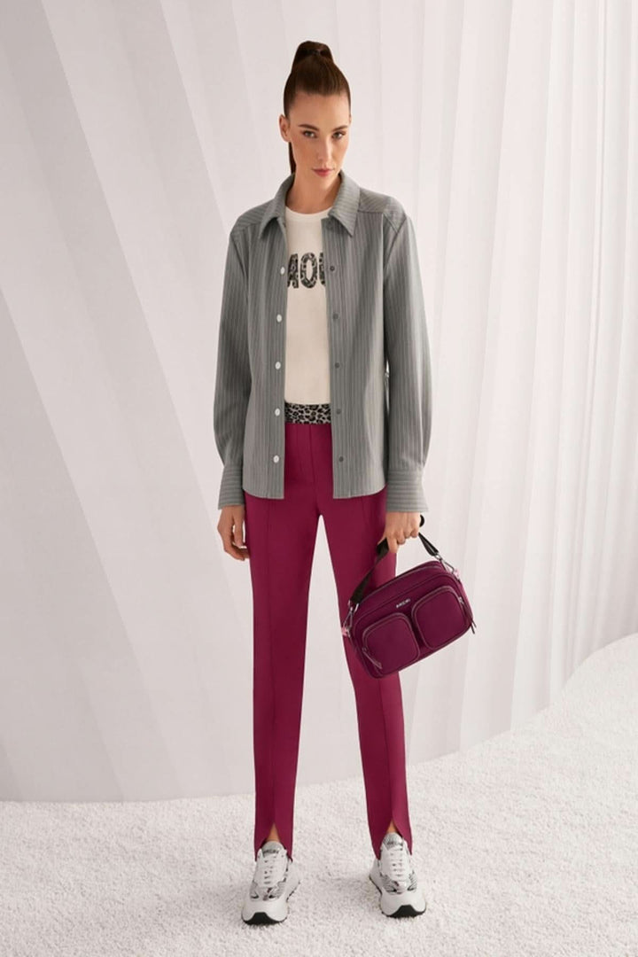 Femme portant une chemise rayée décontractée, avec veste à col et poches, sur un t-shirt graphique. Elle tient un sac à main bordeaux.