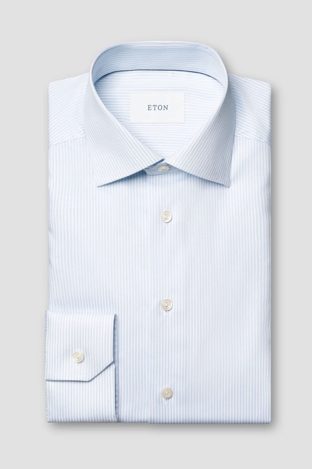 Chemise rayée en coton et lyocell avec fines rayures bleues et col italien structuré, allongée sur un fond gris clair.