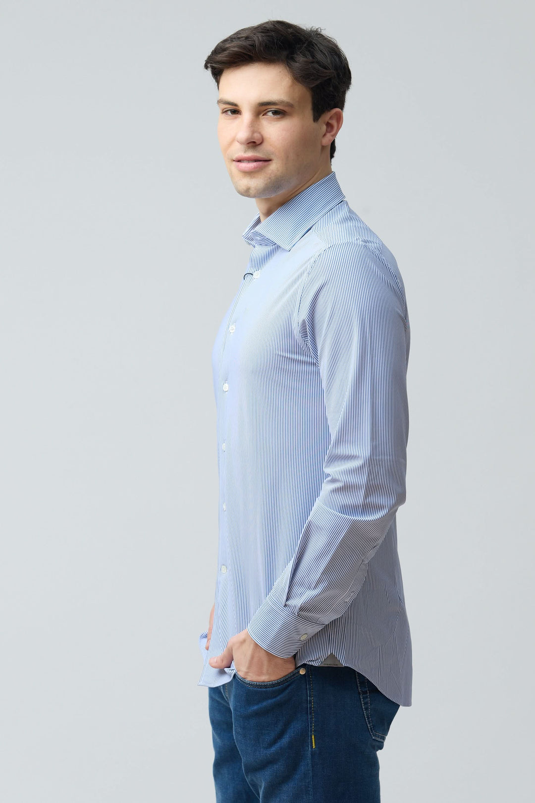 Homme portant une chemise à rayures fines modernes, coupe ajustée, tissu extensible, motif structuré, col classique et fermeture boutonnée.
