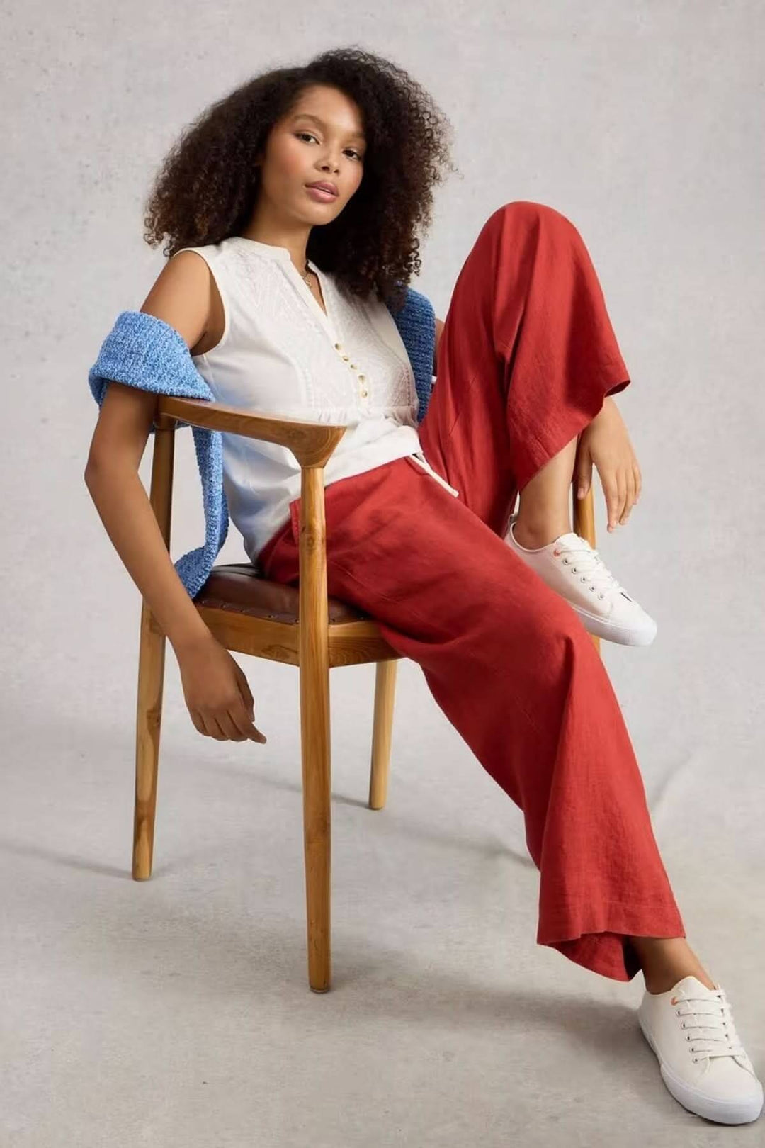 Femme portant la chemise sans manches Peony avec plastron brodé, assise avec pantalon rouge et sneakers blanches, look casual élégant.