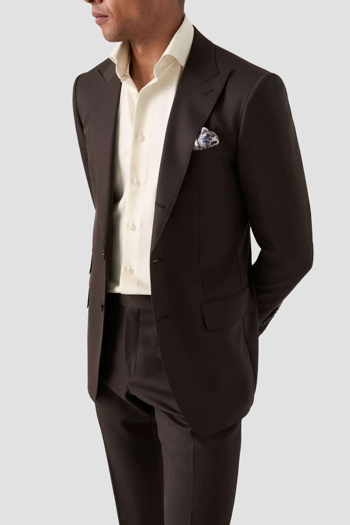 Homme en costume marron élégant avec chemise claire et pochette de costume.
