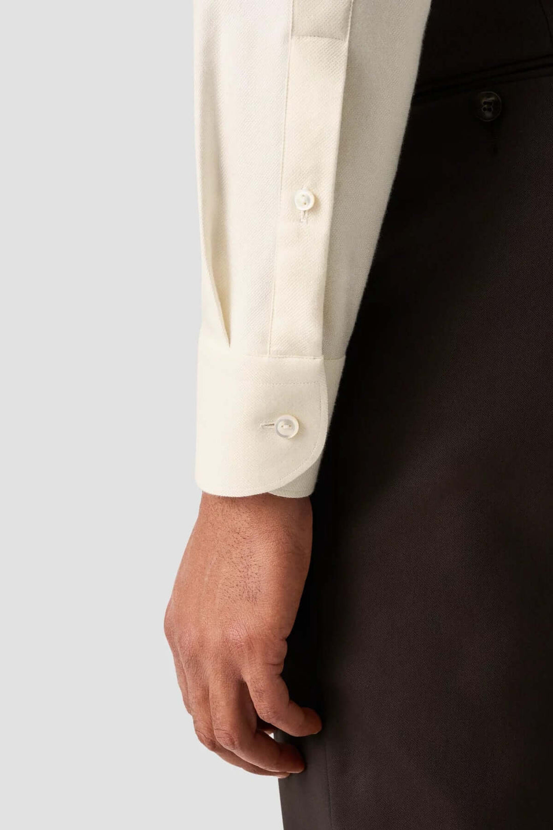 Man’s hand wearing an elegant cream cotton shirt with structured cuffs.