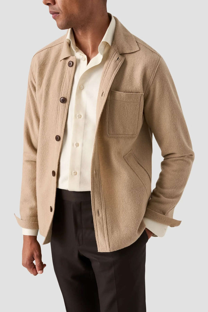 Homme portant une chemise unie en coton avec une veste beige en tissu texturé et des pantalons foncés.