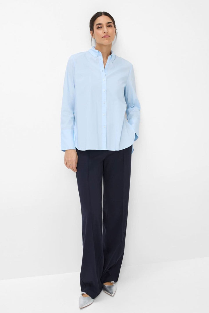 Chemisier classique VIKI en bleu clair, élégant, manches longues et silhouette légèrement évasée, porté avec un pantalon marine.