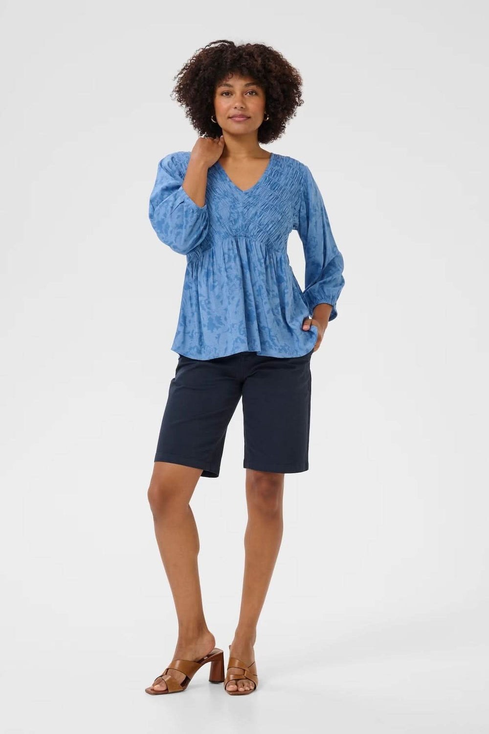 Femme portant un chemisier bleu à col en V et un short noir, affichant une tenue décontractée et stylée.