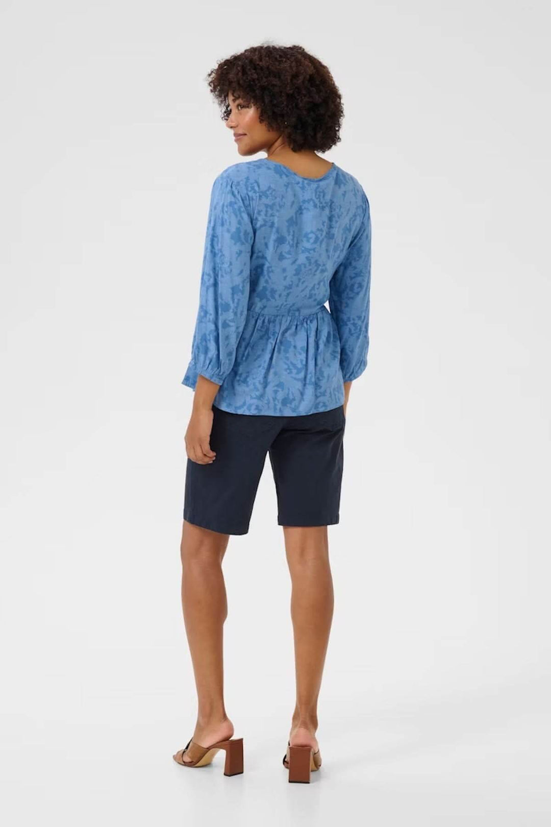Femme portant un chemisier bleu à col rond avec manches longues, vue arrière, associé à un short.