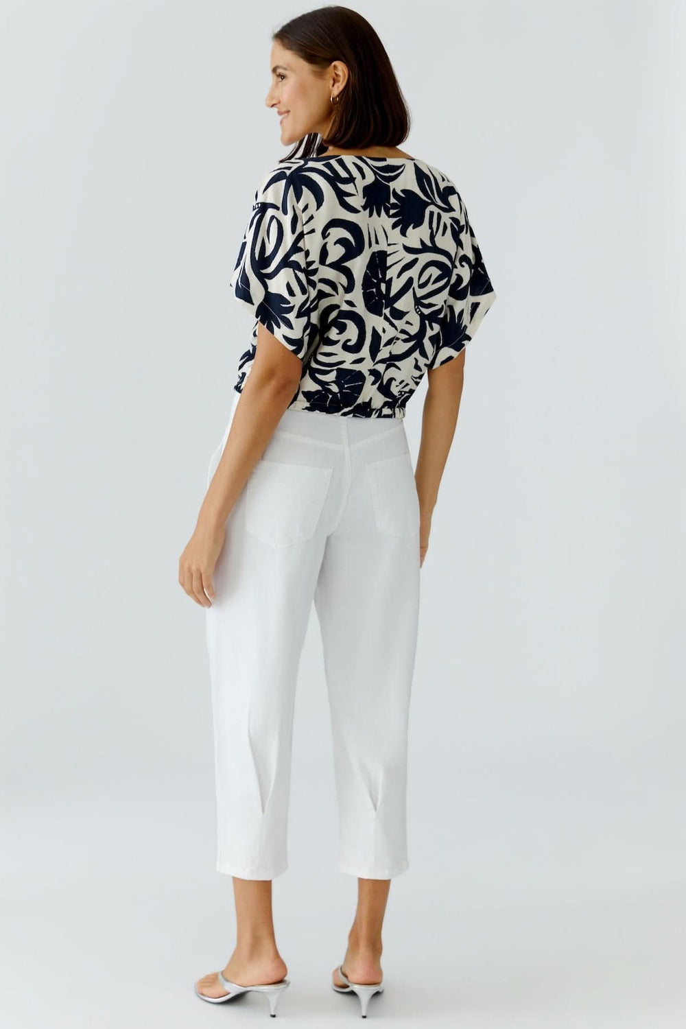 Femme portant un chemisier à manches courtes imprimé artistique avec pantalon blanc, vue de dos.