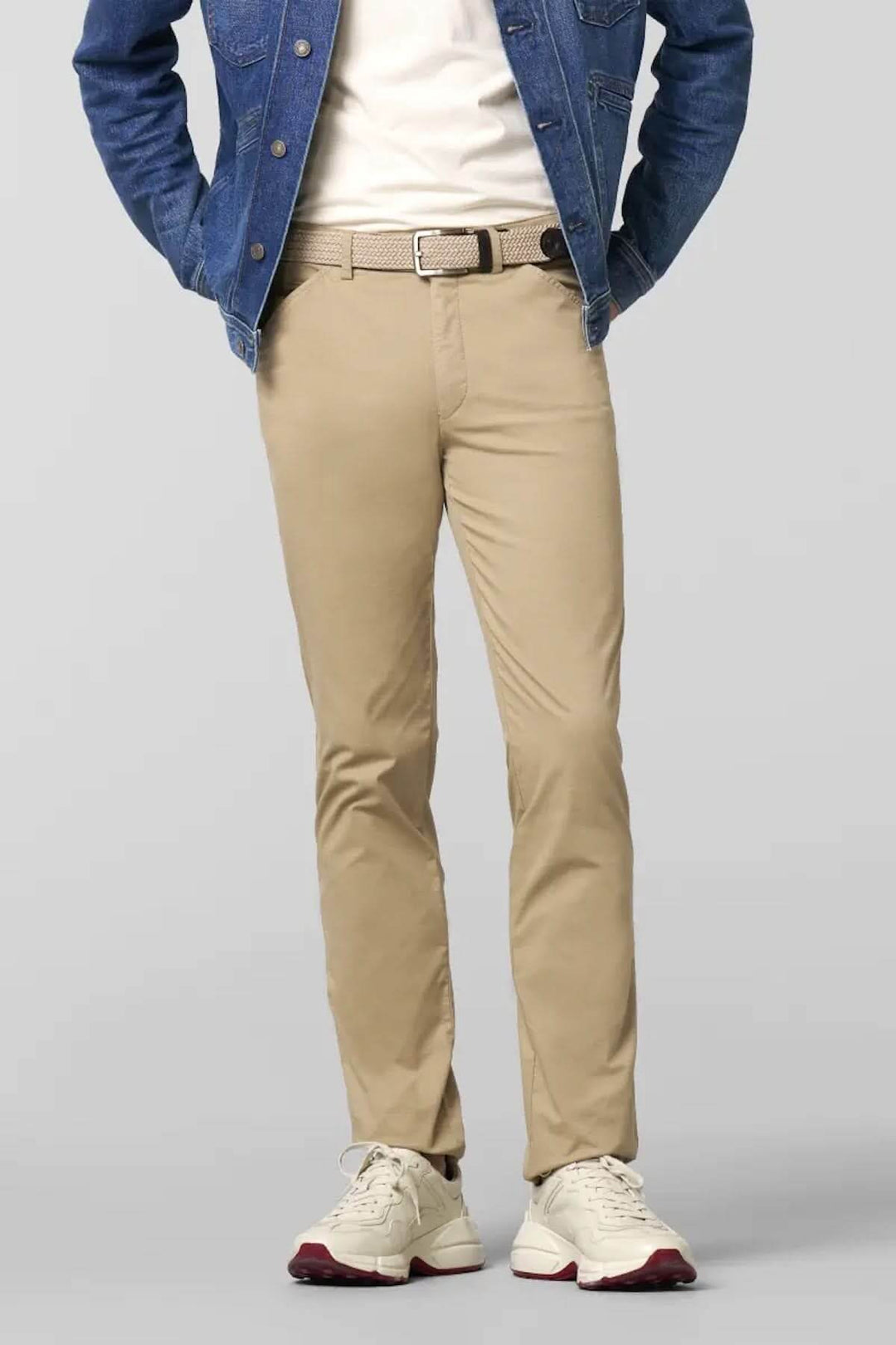 Pantalon chino ajusté beige porté avec un t-shirt blanc et une veste en jean, allié à des baskets blanches.