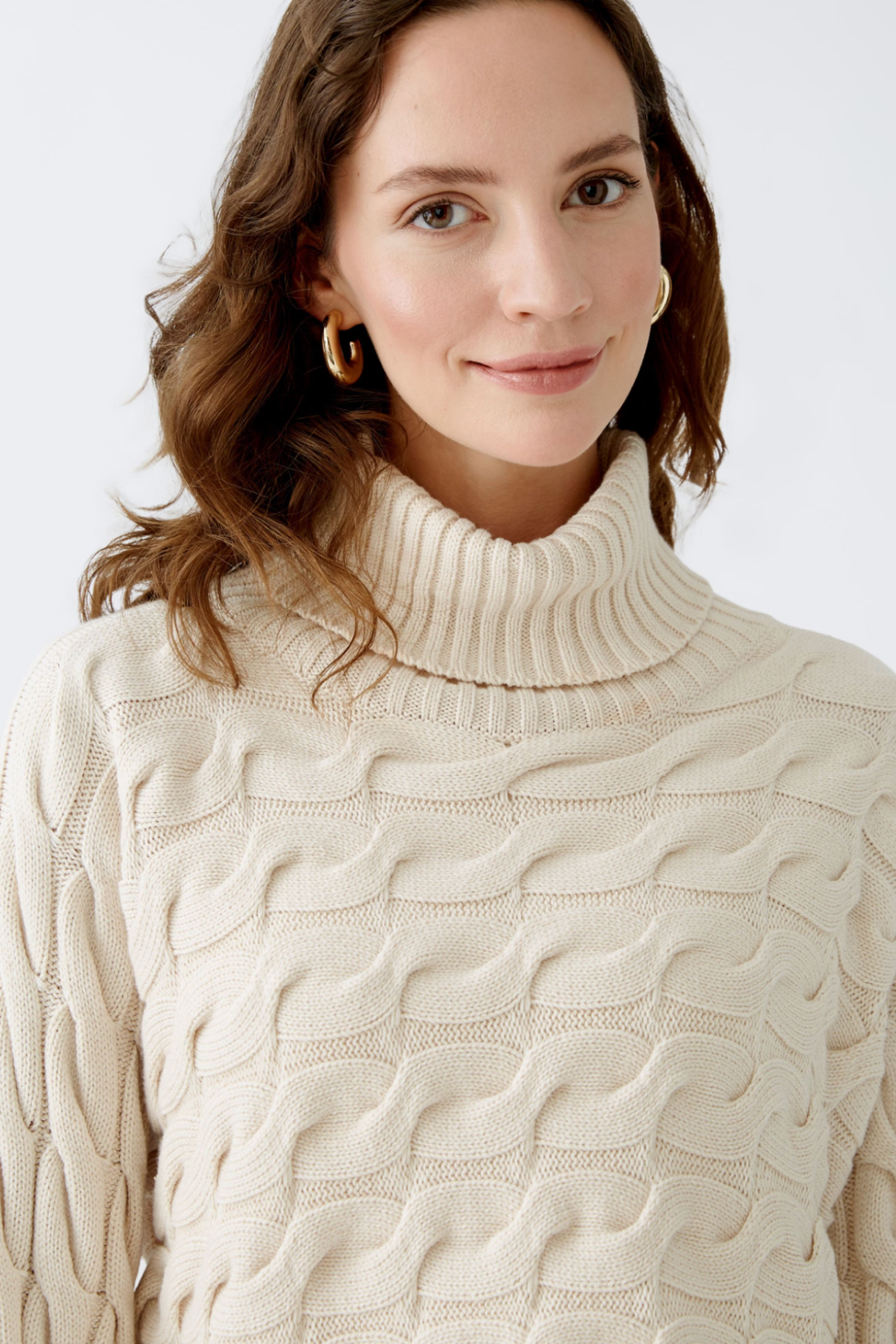 Femme portant un col roulé en tricot torsadé beige, col côtelé, look moderne et élégant.