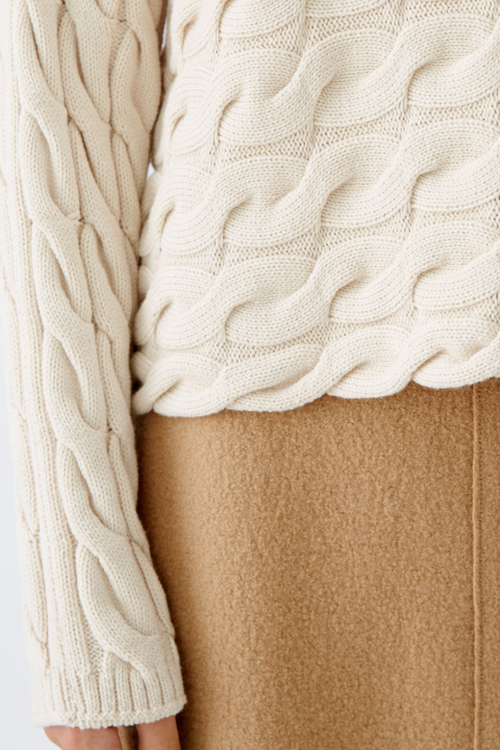 Col roulé en tricot torsadé beige avec un pantalon beige, alliant confort et élégance pour un look hivernal.