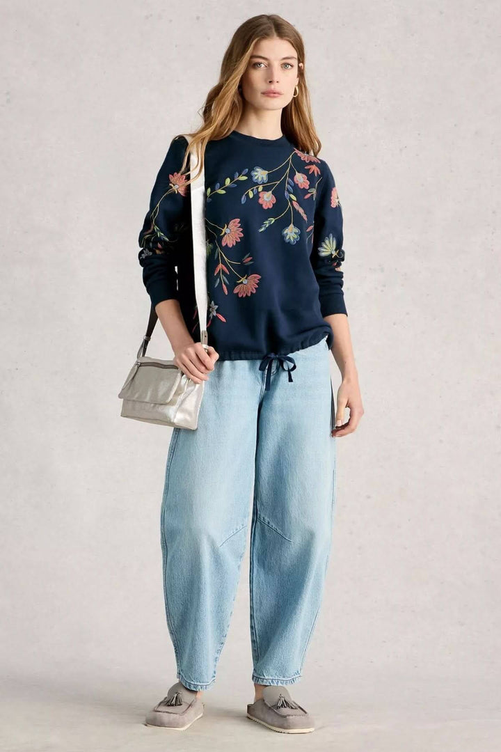 Femme portant un coton ouaté à broderie florale, style décontracté avec un jean ample, parfait pour la mi-saison.