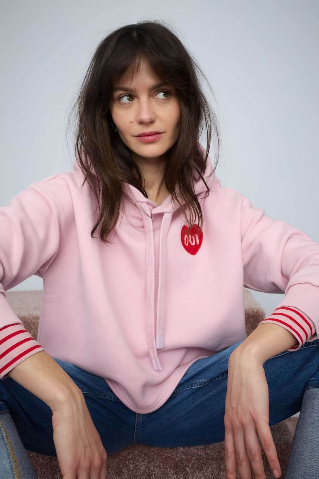 Femme portant un coton ouaté à capuche avec écusson cœur 'OUI', assise en jean, style décontracté moderne.