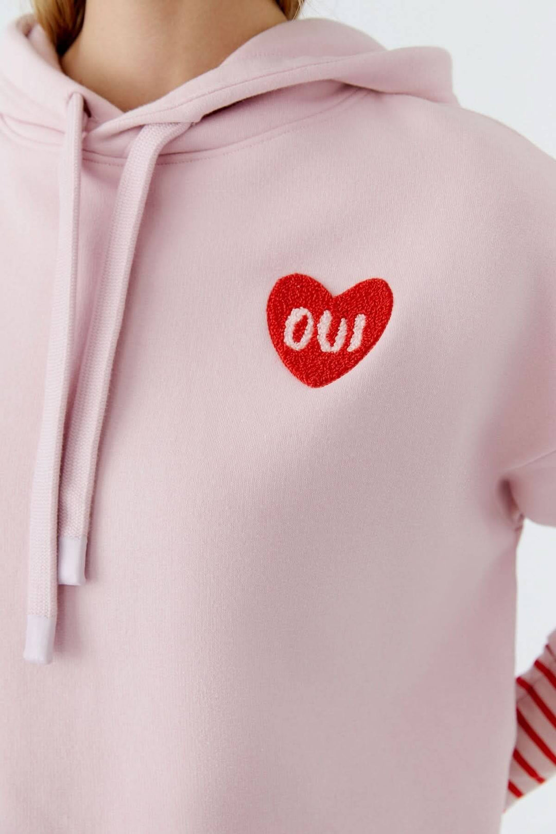 Coton ouaté à capuche avec écusson cœur rouge « OUI » brodé sur la poitrine, offrant un look décontracté et moderne.