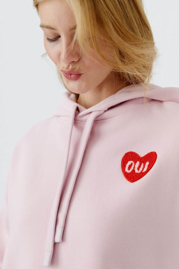 Coton ouaté à capuche avec écusson cœur "OUI" brodé, femme portant le vêtement rose pour un look décontracté.
