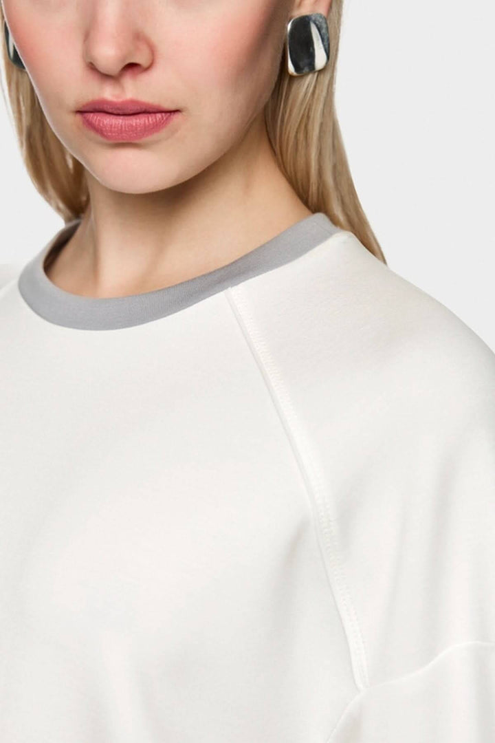 Femme portant un coton ouaté décontracté blanc avec col gris et manches bouffantes. Logo Marc Cain Sports visible.