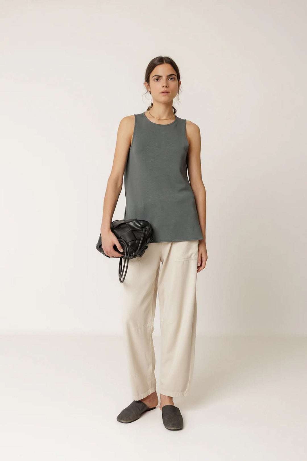 Femme portant un débardeur minimaliste à coupe fluide avec un pantalon blanc, tenant un sac noir.