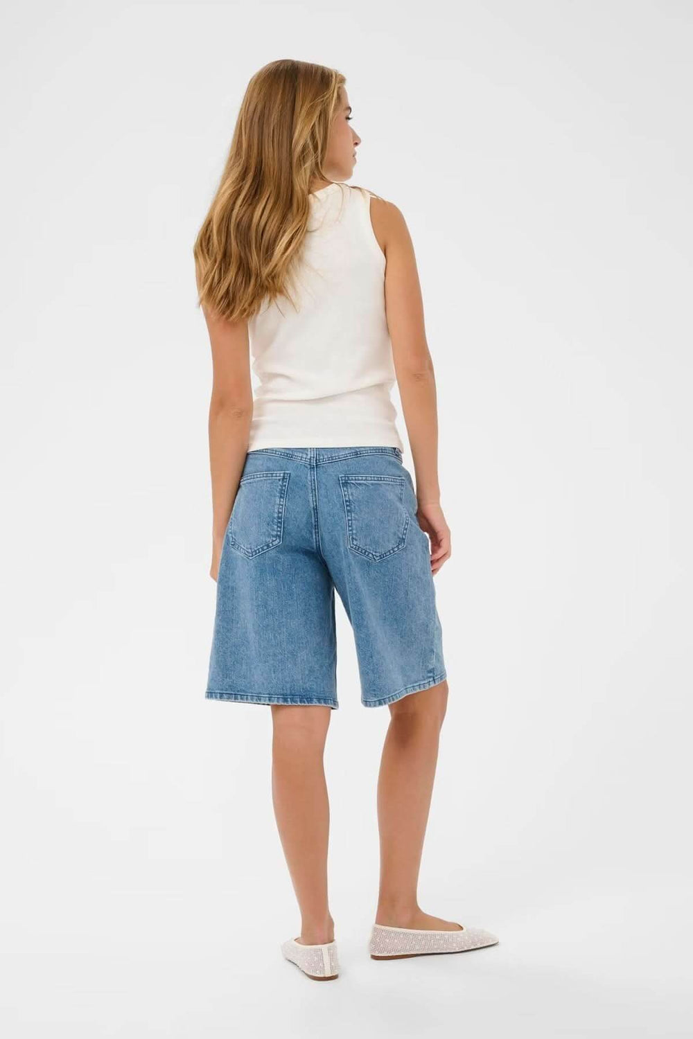 Femme de dos portant un débardeur sans manches en coton blanc avec jean, montrant coupe ajustée et élégante, style casual chic.