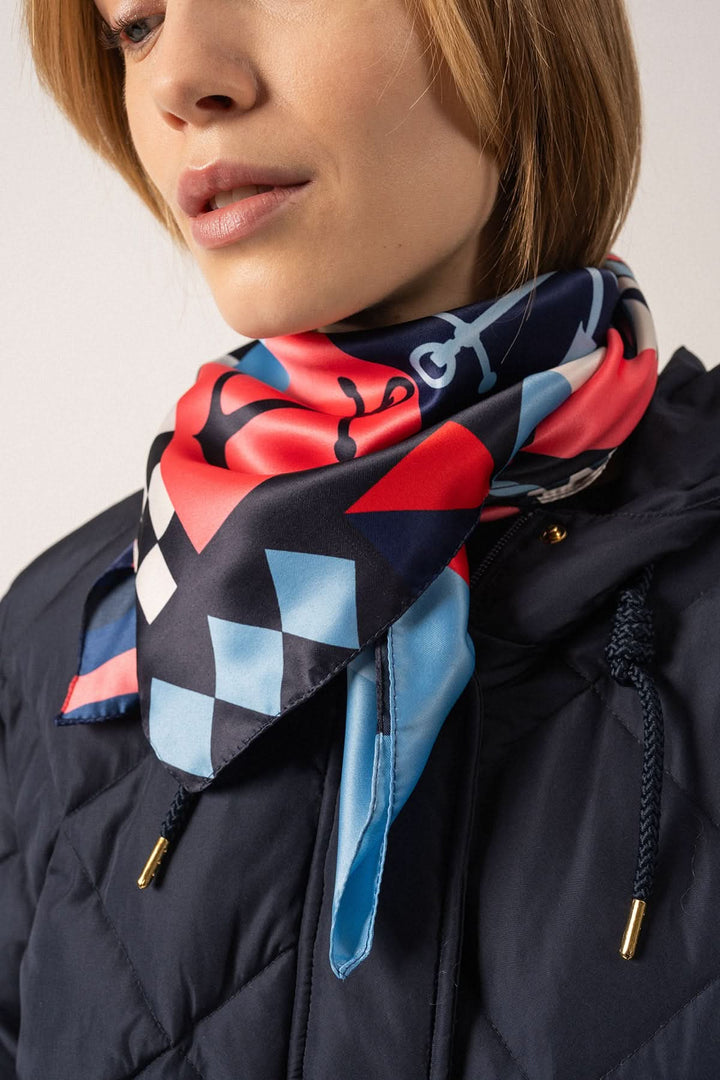 Foulard carré marine porté avec élégance, motif coloré sur fond noir, ajoutant une touche nautique au style.