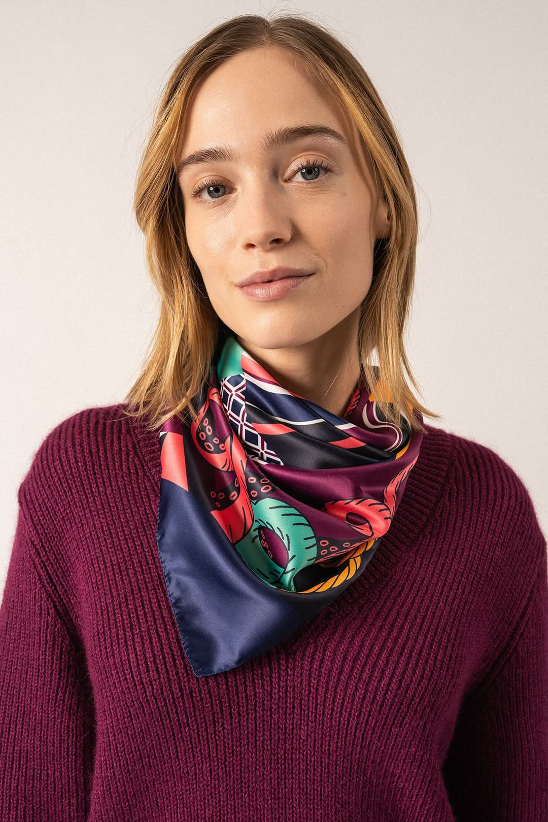 Foulard carré fond marin porté par femme avec motif nautique, couleur vive et élégante, dimensions 90x90 cm.