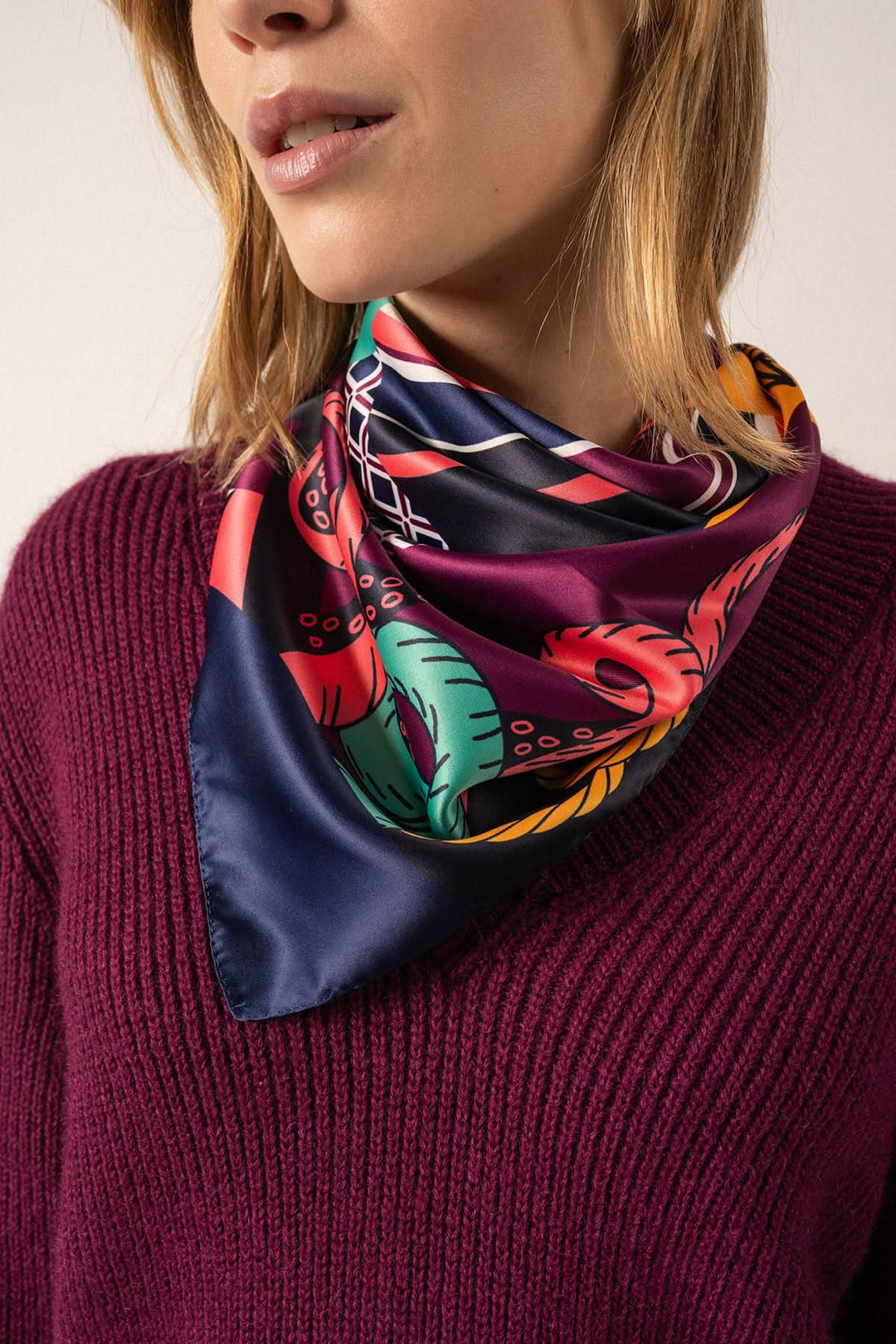 Foulard carré en satin à motifs colorés porté par une femme, style élégant et nautique.