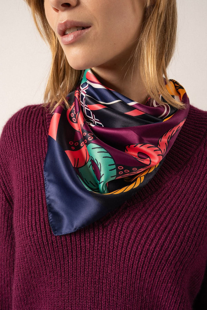 Foulard carré en satin à motifs colorés porté par une femme, style élégant et nautique.