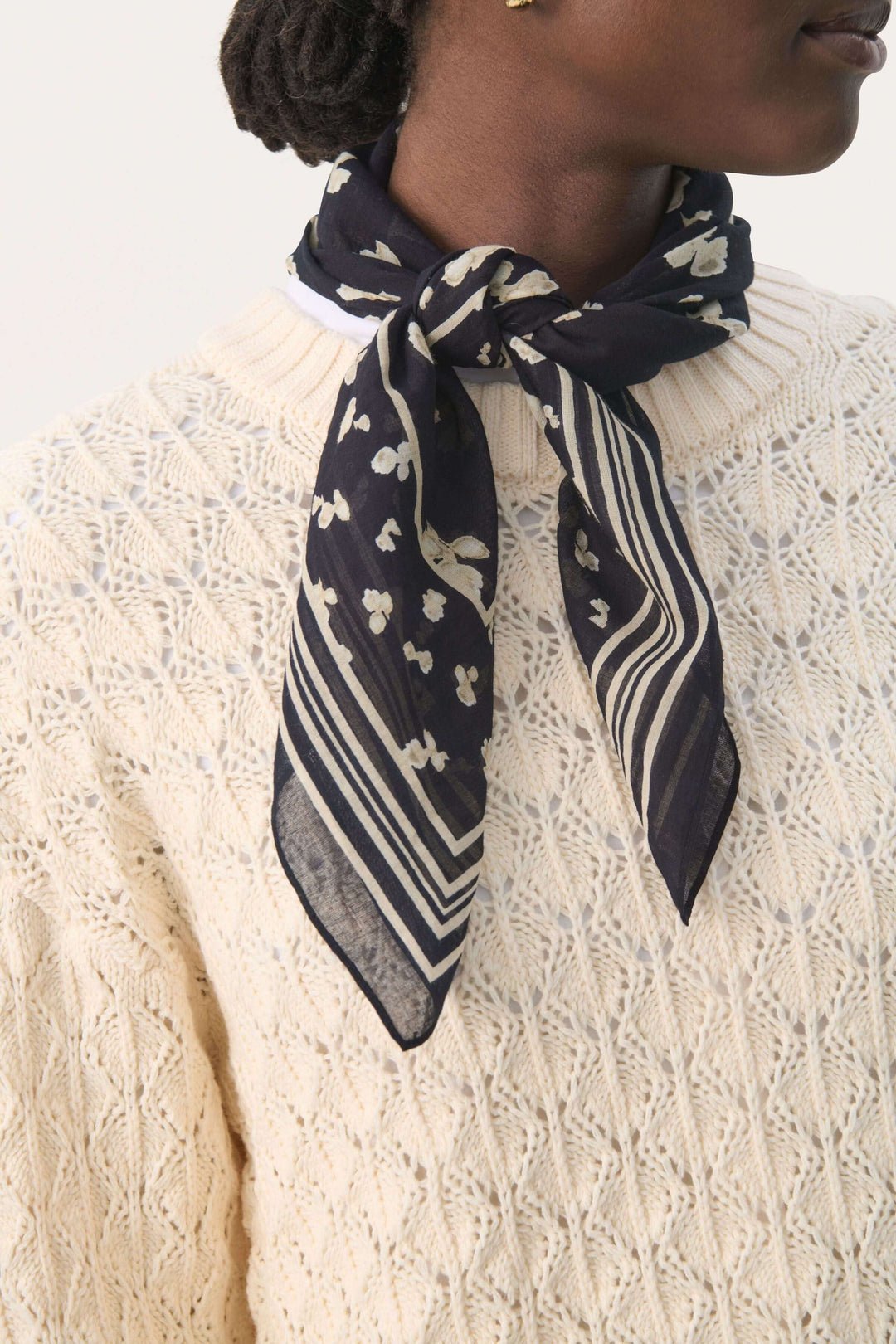 Foulard Phi élégant avec motifs délicats, porté autour du cou sur un pull en maille beige.