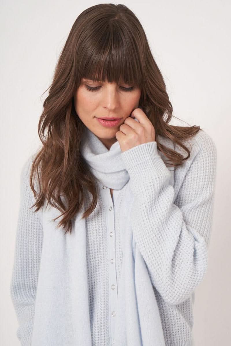 Femme portant un foulard doux essentiel gris clair, drapé élégamment autour du cou, combiné à un pull texturé.