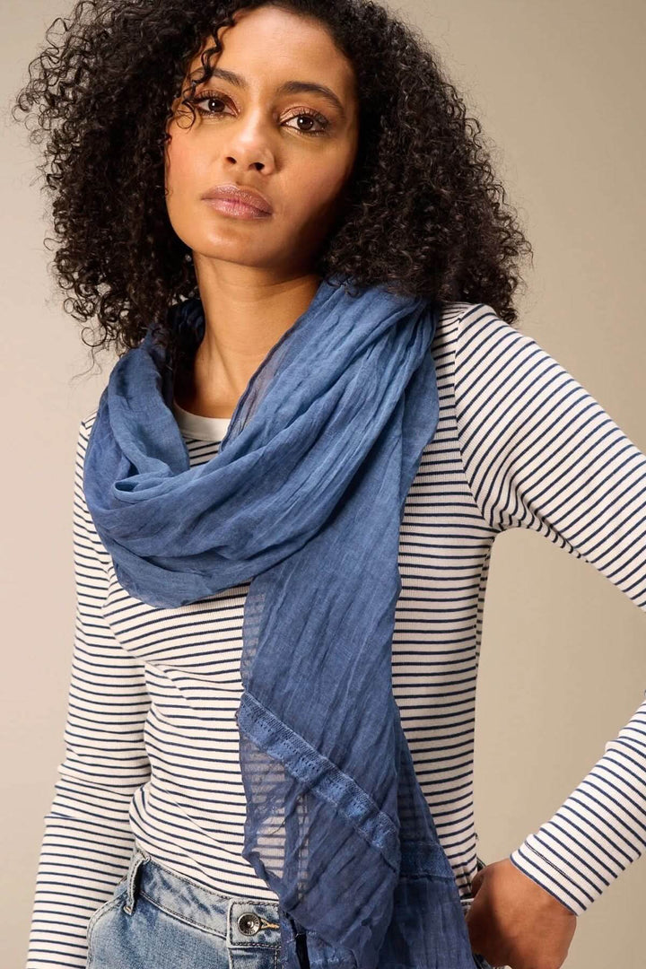 Foulard en coton bleu léger et fluide porté autour du cou d'une femme, ajoutant une touche de douceur et d'élégance à sa tenue.