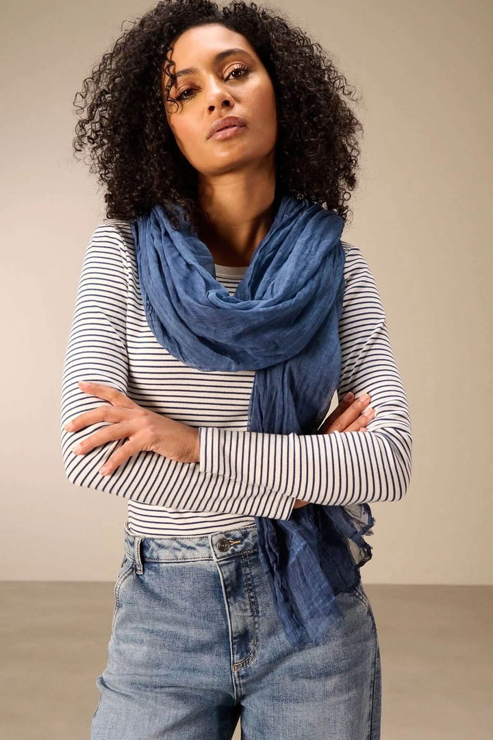 Foulard en coton bleu porté par une femme sur un pull rayé pour un look naturel et élégant