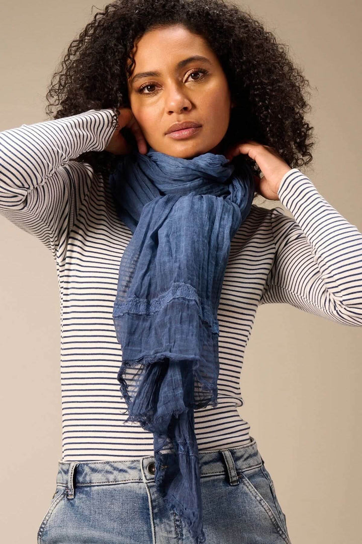 Femme portant un foulard en coton bleu léger, idéal pour ajouter une touche de douceur et d'élégance à une tenue décontractée.