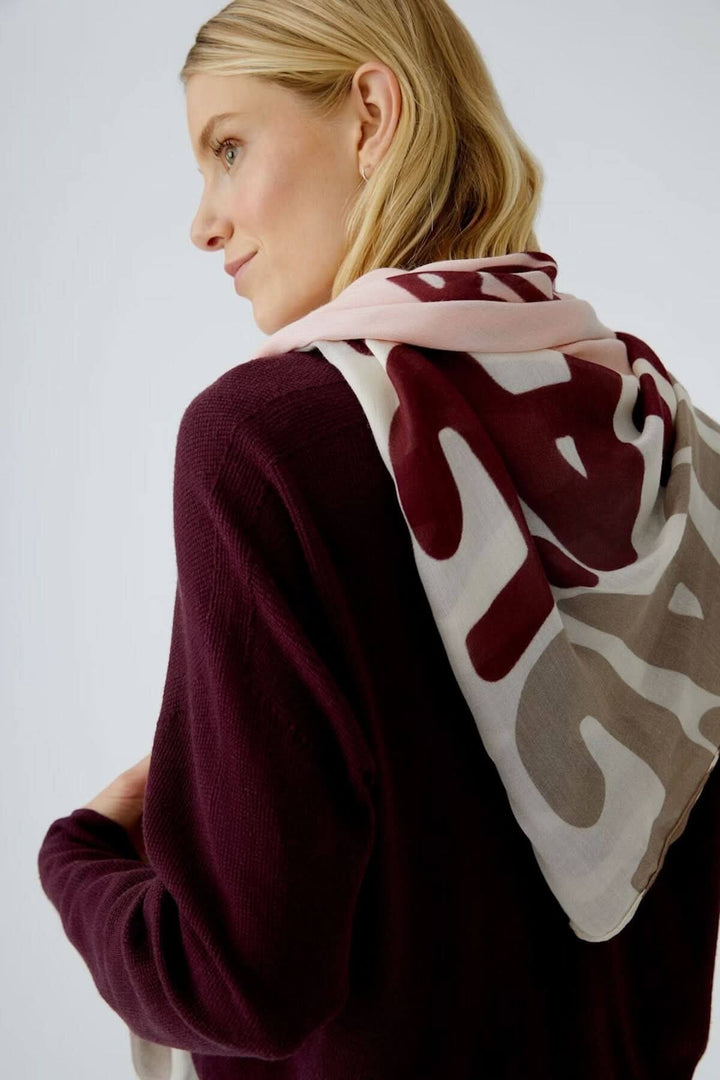 Foulard en voile léger avec imprimé artistique multicolore, noué autour du cou d'une femme en pull bordeaux, chic et polyvalent.