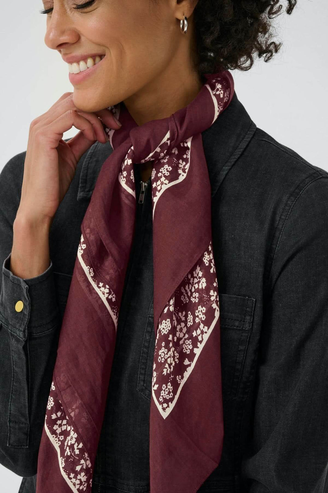 Foulard à motif fleuri Loui au cou, couleur bordeaux avec bordure contrastante, idéal pour un style sophistiqué et polyvalent.