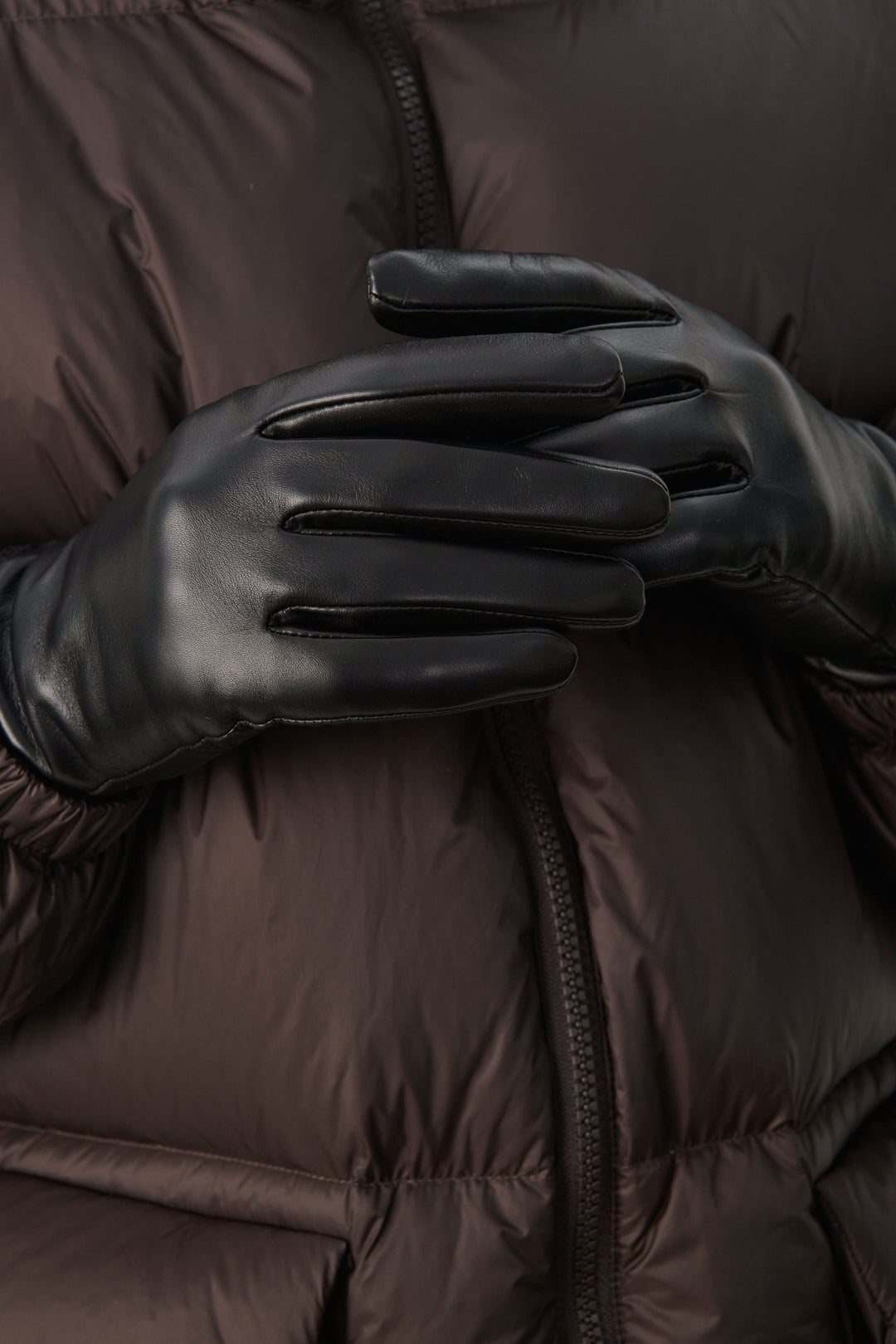 Gants en cuir noir, élégants et ajustés, parés pour les journées froides, avec une doudoune brune.