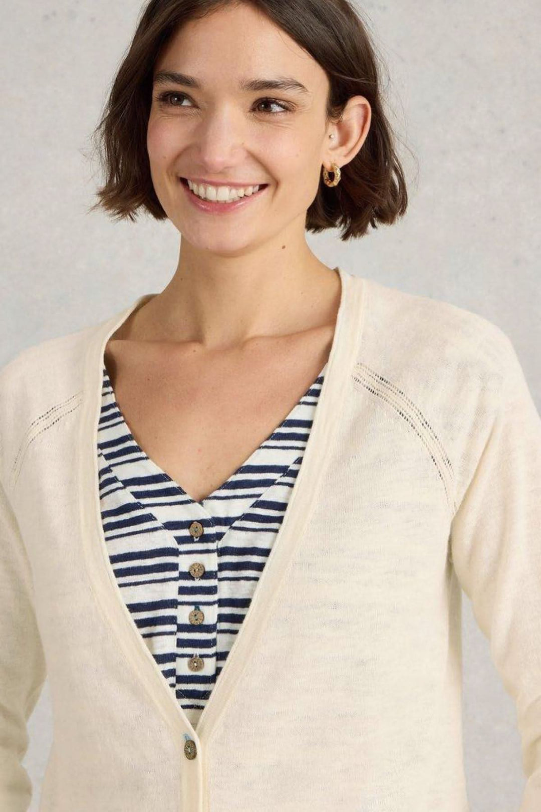 Femme souriante portant un gilet blanc cassé à encolure en V avec un haut à rayures dessous.