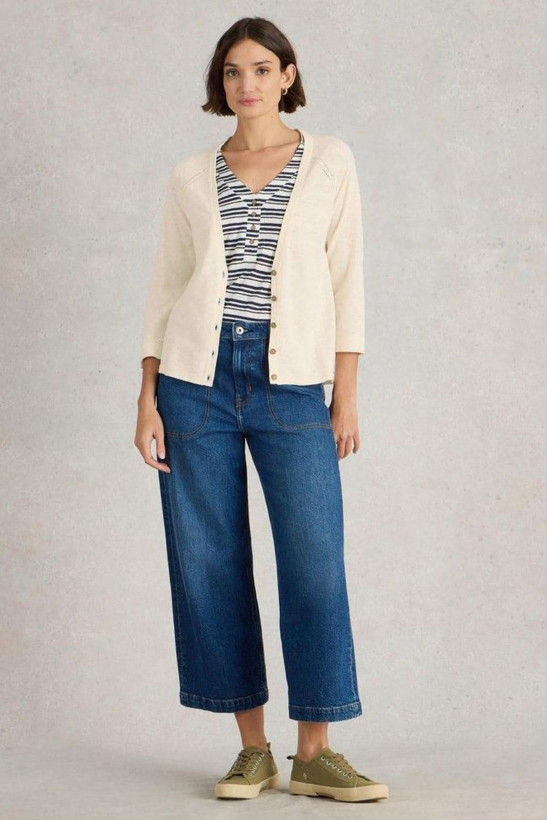 Modèle portant un gilet col V blanc cassé, jeans larges et baskets, pour un look décontracté élégant.