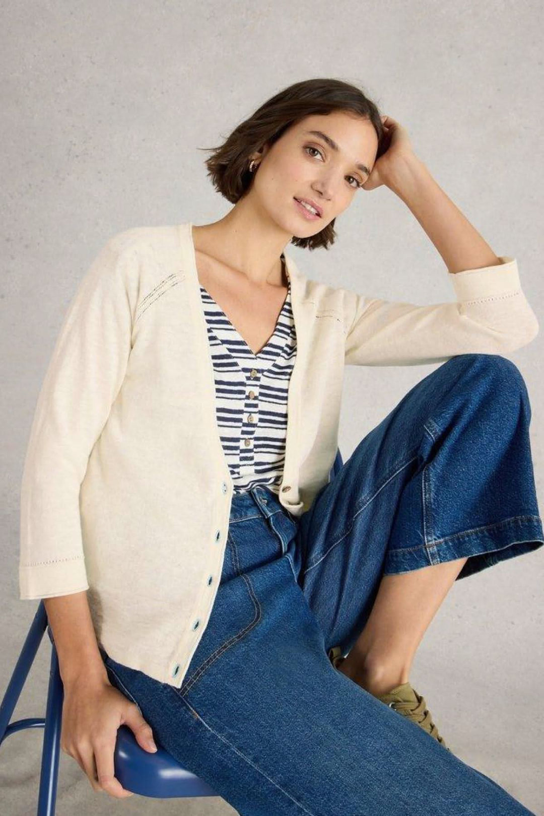 Femme portant un gilet Col V Naria blanc cassé avec une tenue décontractée en jeans et haut rayé.