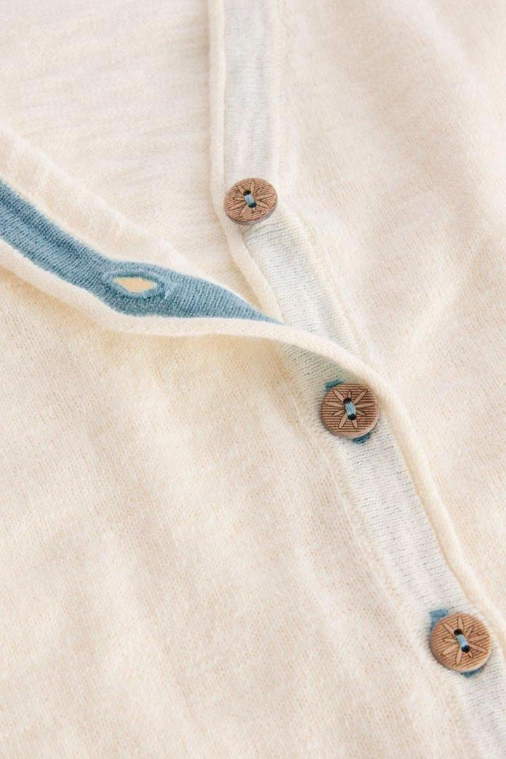 Gilet Col V Naria, blanc cassé, avec boutons marron et bordure intérieure bleue.