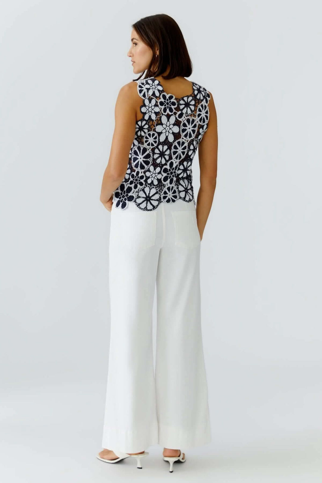 Femme portant un haut coupe moderne minimaliste noir avec dos en dentelle florale, associé à un pantalon blanc fluide pour une allure élégante.