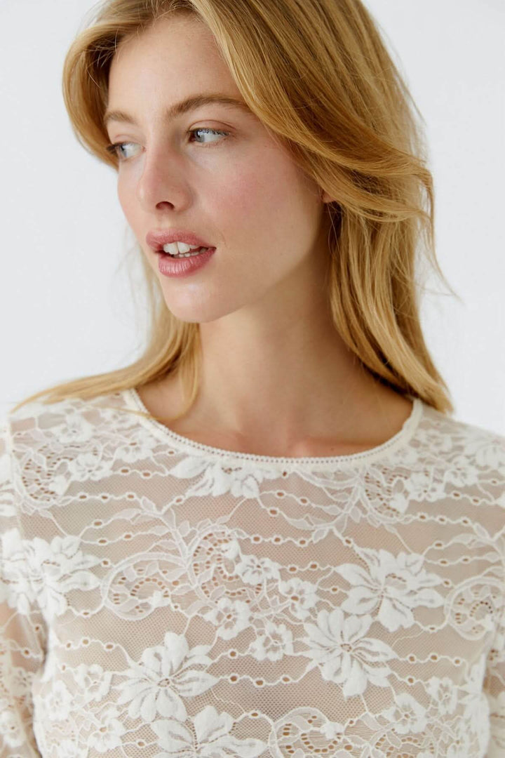 Femme portant un haut en dentelle florale blanc, mettant en valeur une silhouette élégante et raffinée.