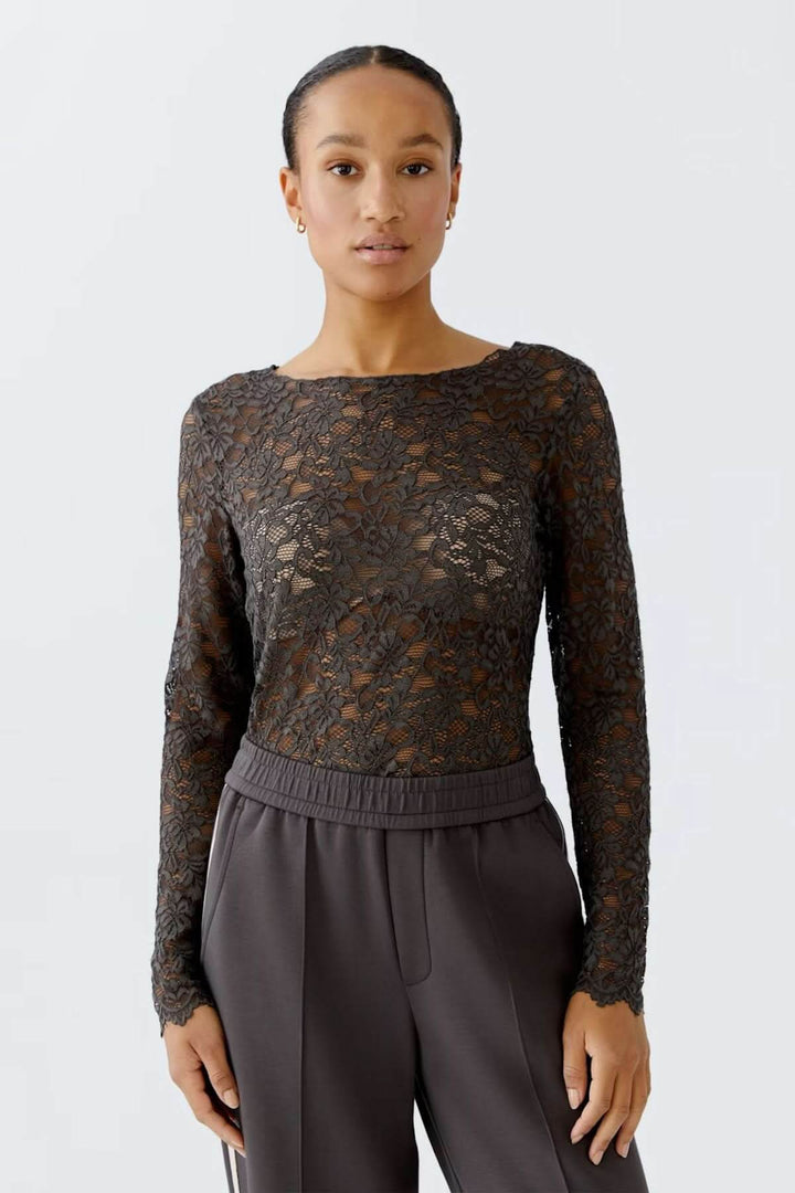 Femme portant un haut en dentelle florale à manches longues et encolure bateau, coupe ajustée et moderne. Parfait avec un pantalon habillé.