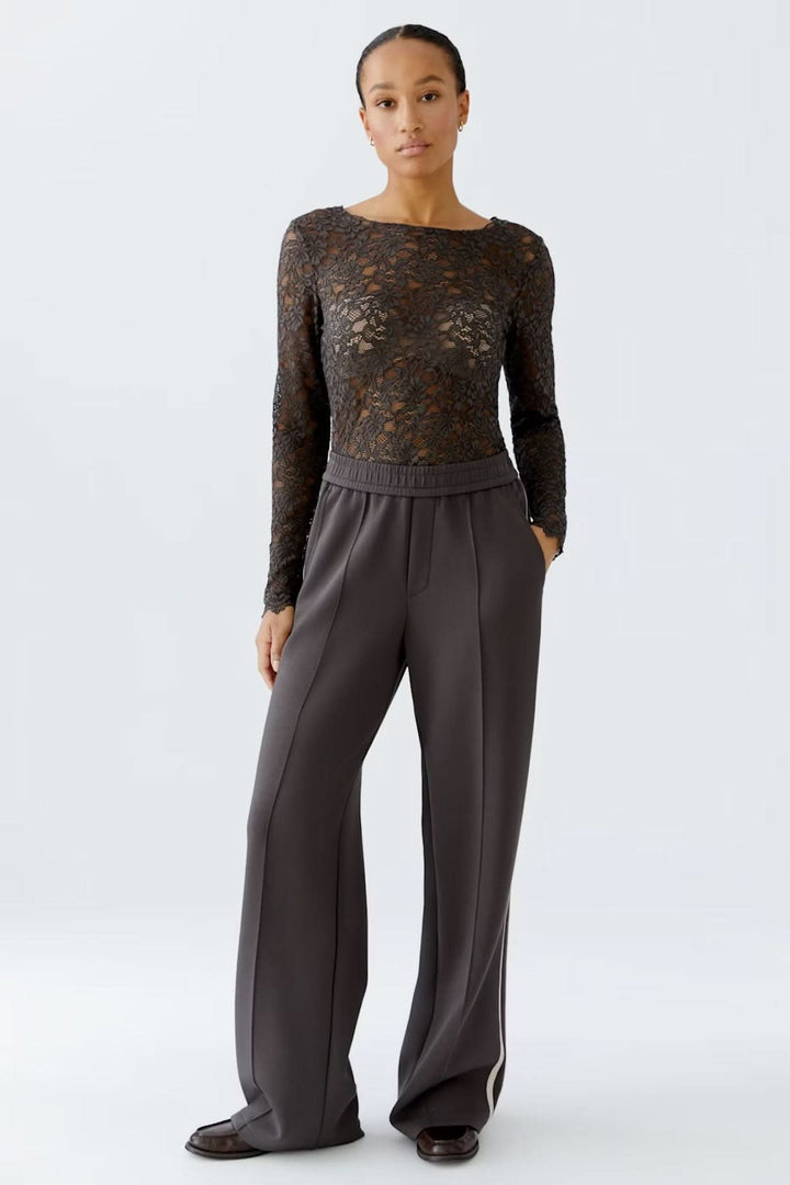 Femme portant un haut en dentelle florale ajusté avec manches longues et encolure bateau, associé à un pantalon habillé.