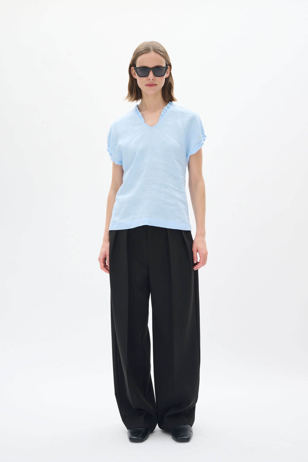 Haut en lin Rigitta à encolure en V, manches courtes, porté avec un pantalon noir, parfait pour l'été.