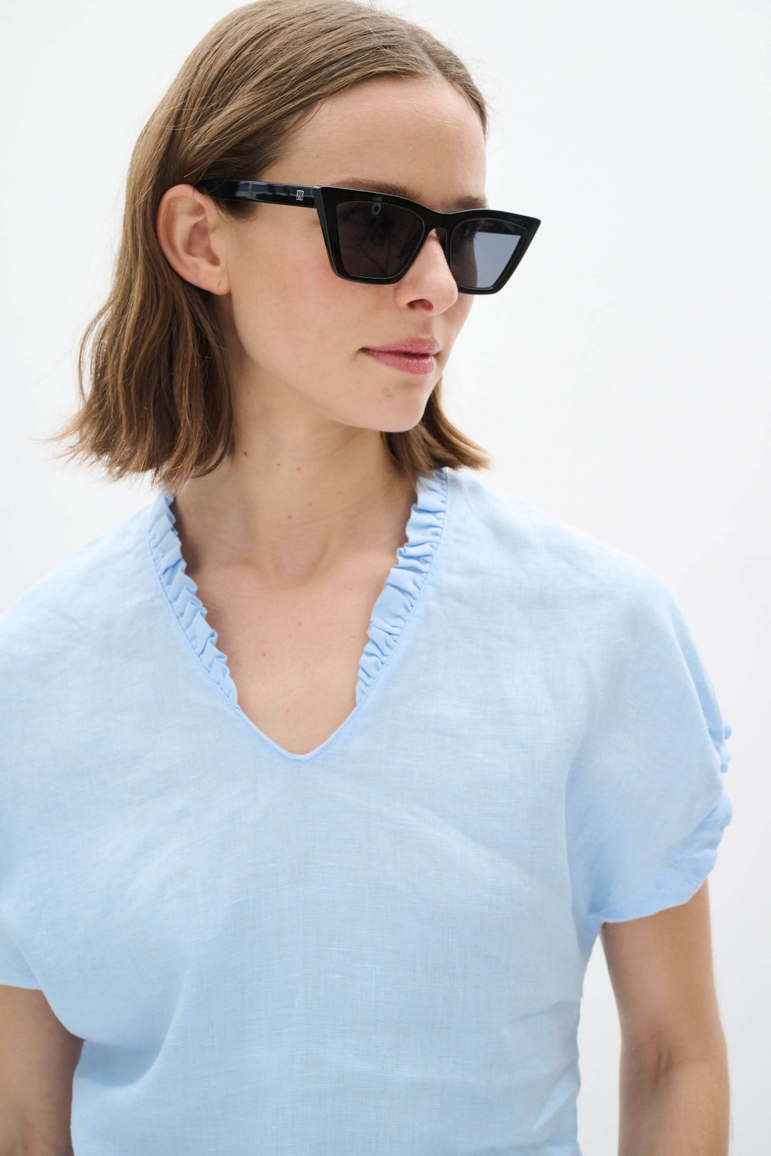 Femme portant un haut en lin bleu clair avec encolure en V et lunettes de soleil noires.