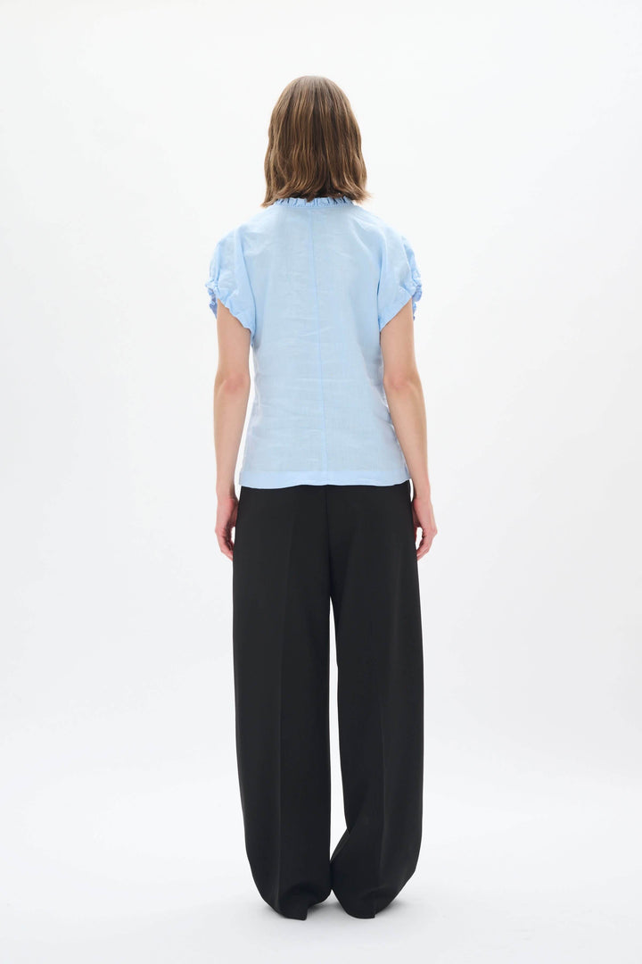 Haut en lin bleu clair vu de dos avec pantalon noir, style décontracté et élégant pour l'été.