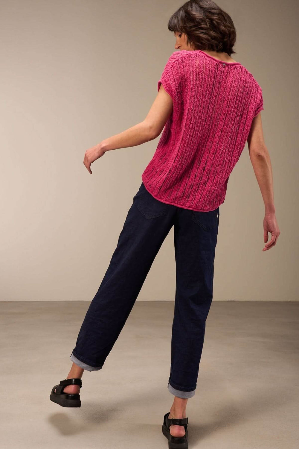 Femme portant un haut en maille ajourée rose avec un pantalon noir, parfait pour un style décontracté estival.