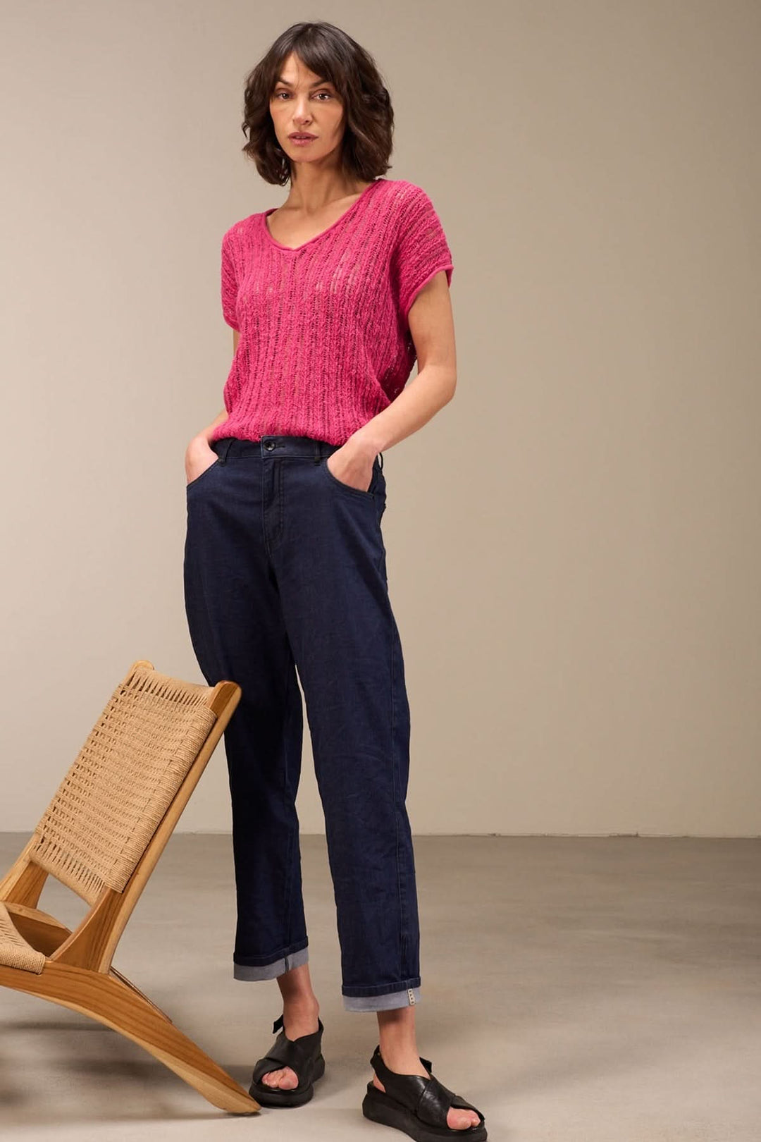 Femme portant un haut en maille ajourée rose et un pantalon bleu, dans un intérieur moderne.